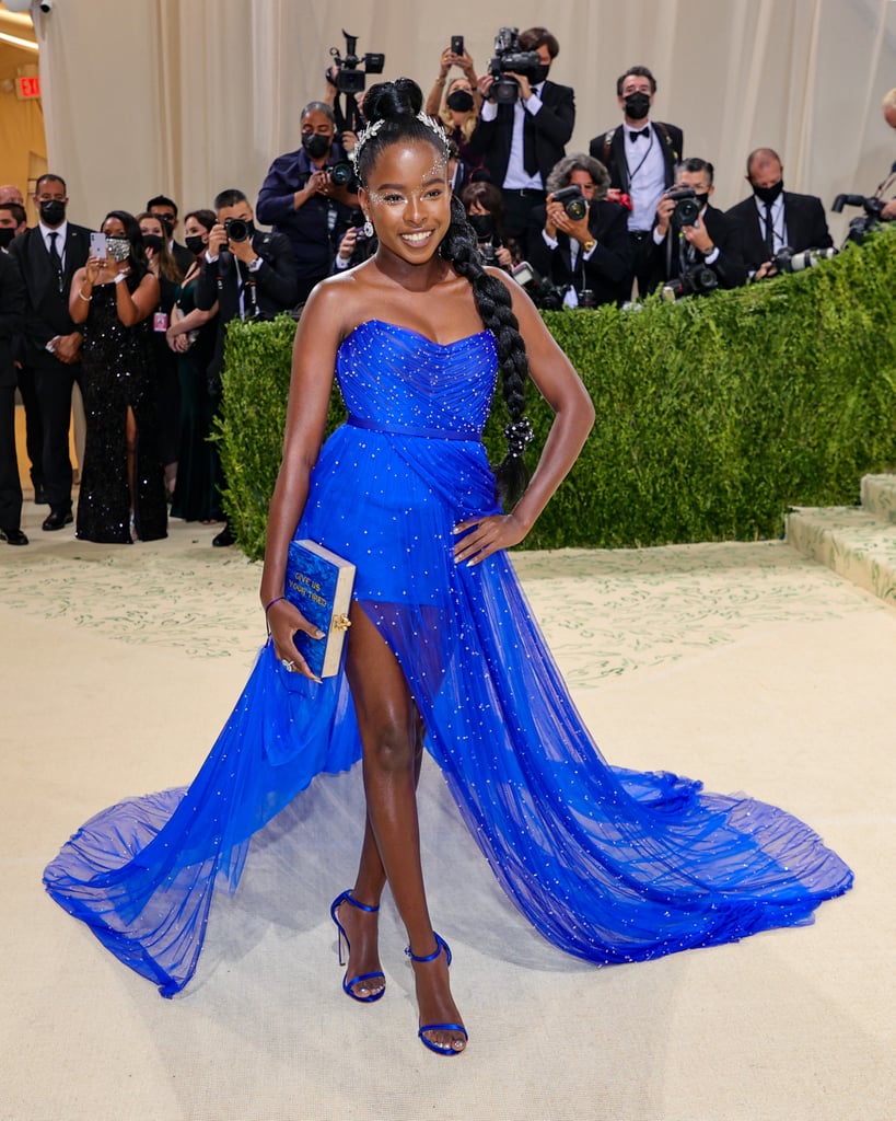 Amanda Gorman is a vision in blue! She wowed the nation at the presidential inauguration earlier the year with her beautiful poem  and gorgeous Prada coat, and she did it again at her first-ever Met Gala Monday night. Wearing a royal blue Vera Wang minidress featuring a dramatic long train adorned with little pearls — as well as matching Stuart Weitzman sandals — the newcomer dazzled on the red carpet. 
While Amanda certainly looked incredible, the meaning behind her look is even more beautiful: the dress is inspired by the Statue of Liberty, as is her blue book-shaped clutch. Upon closer viewing, the front of her purse reads "Give us your tired," which is a nod to "The New Colossus" poem on display inside the landmark. See the 23-year-old poet, who's co-chairing the event alongside Timothée Chalamet, Billie Eilish, and Naomi Osaka, posing from all angles ahead.

    Related:

            
            
                                    
                            

            Amanda Gorman&apos;s Met Gala Hairstyle Has a Tiny Detail With Huge Significance