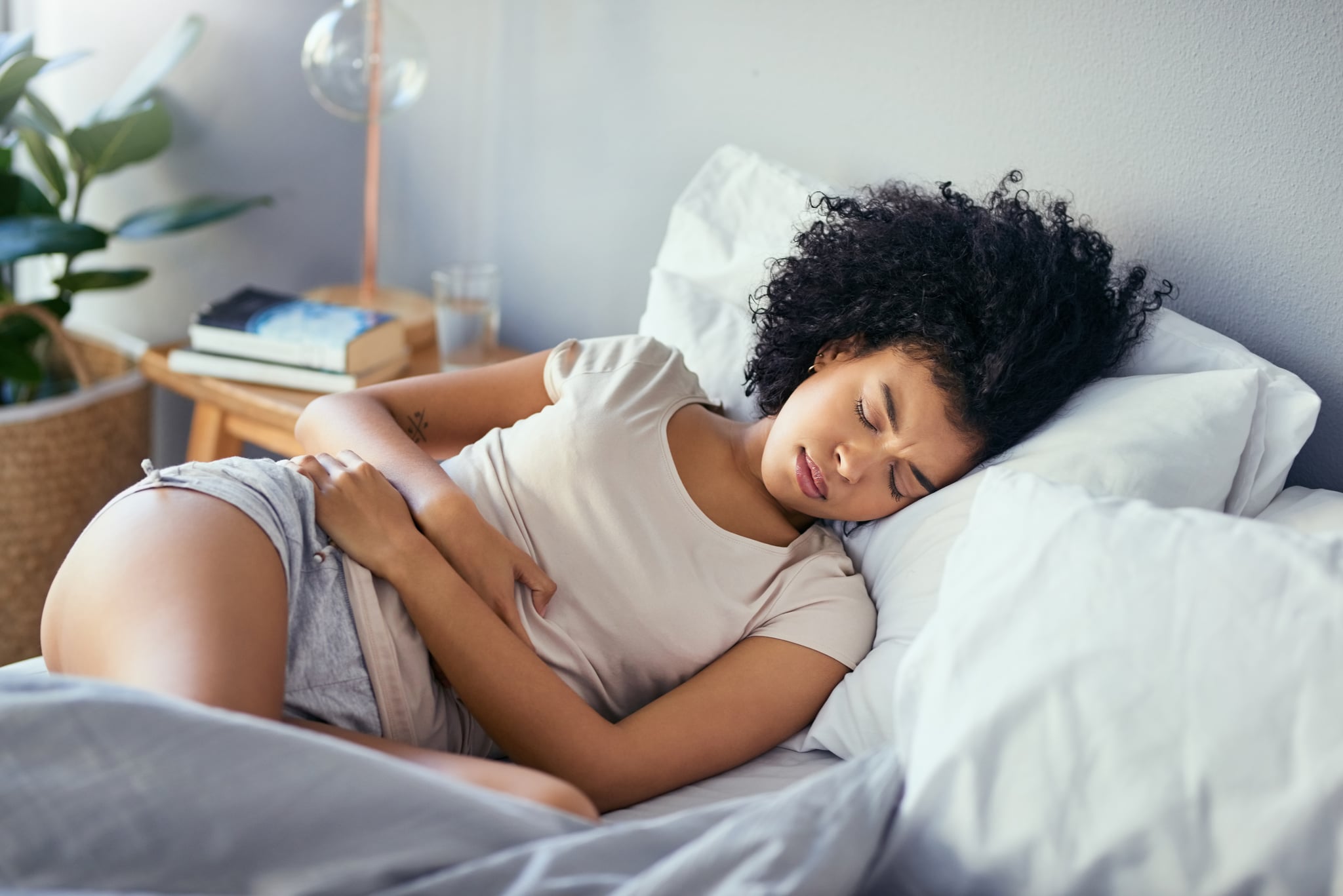 Shot of a young woman suffering from stomach cramps in her bedroom