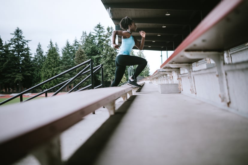 A young woman does sprints up and down the stadium stairs to build speed and strength, training for her next track meet. Horizontal image with copy space.