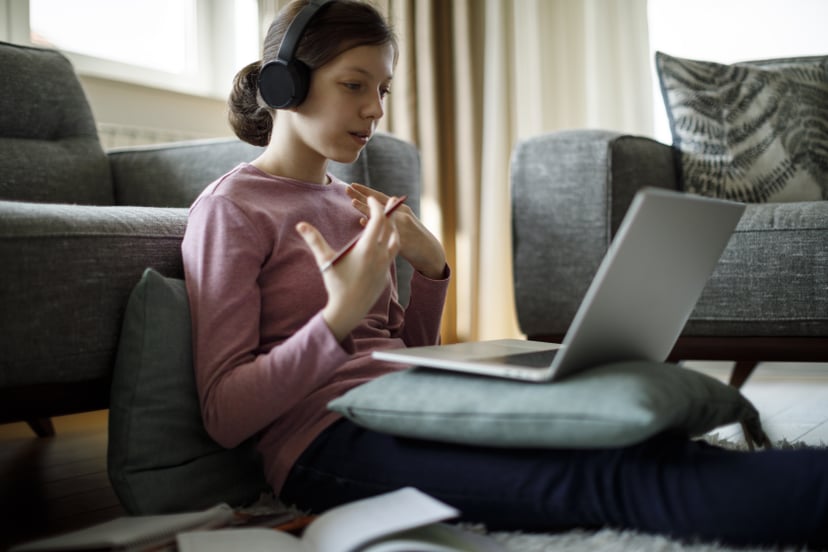 Teenage girl with headphones and laptop having online school class at home