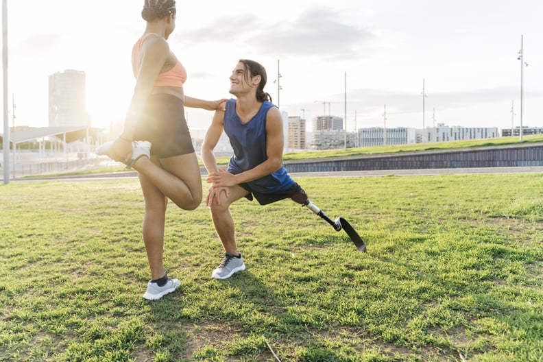 Couple of joggers, one with a prosthetic leg, stretching in a public park on the outskirts of the city at sunset.