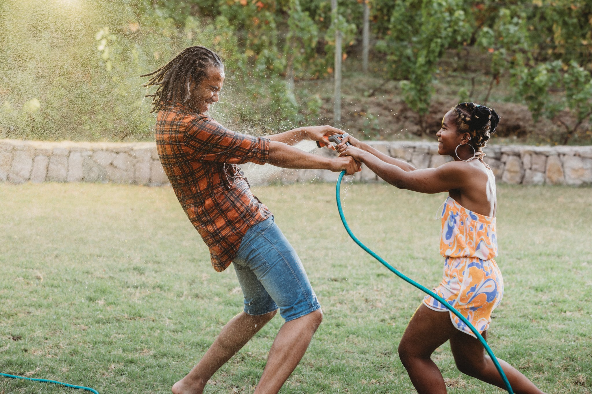 Beautiful young couple playing tug of war with sprinkler hose