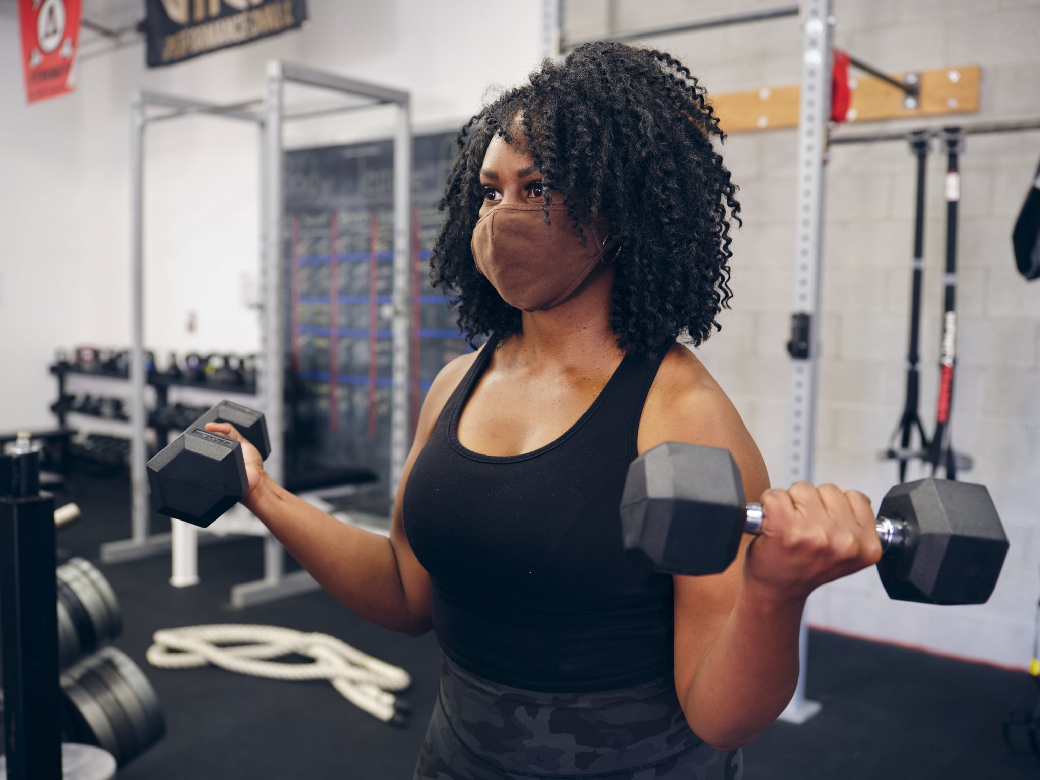 A woman working with a weightlifting equipment in a gym, while wearing a face mask.