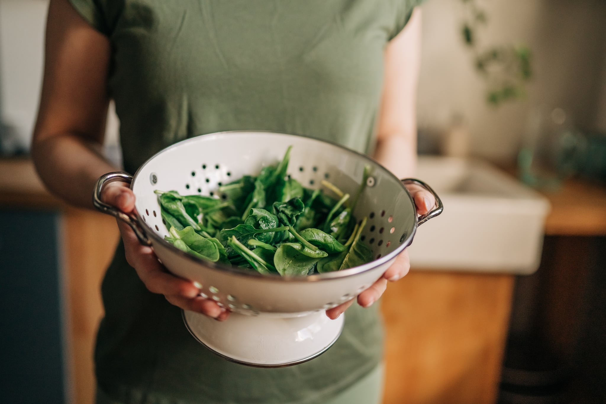 Green vegan breakfast meal in bowl with spinach, arugula, avocado, seeds and sprouts. Girl in leggins holding plate with hands visible, top view. Clean eating, dieting, vegan food concept