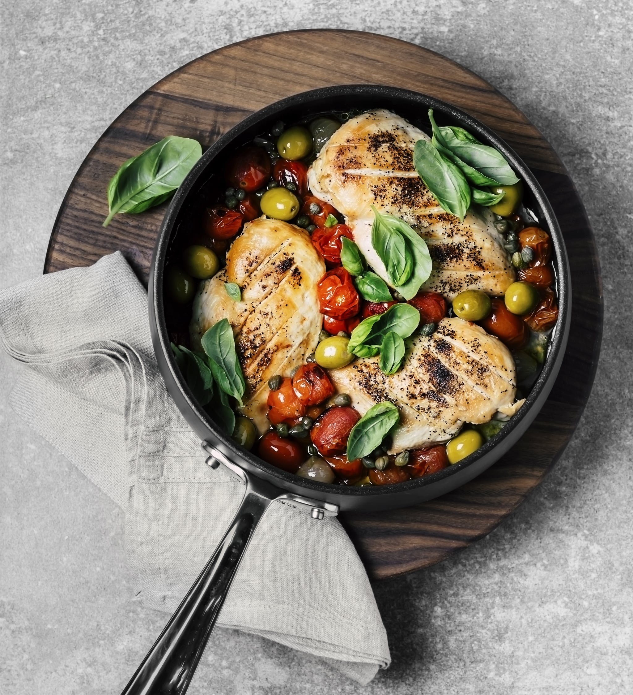 A cooking pan with chicken stew on wooden cutting board on grey background