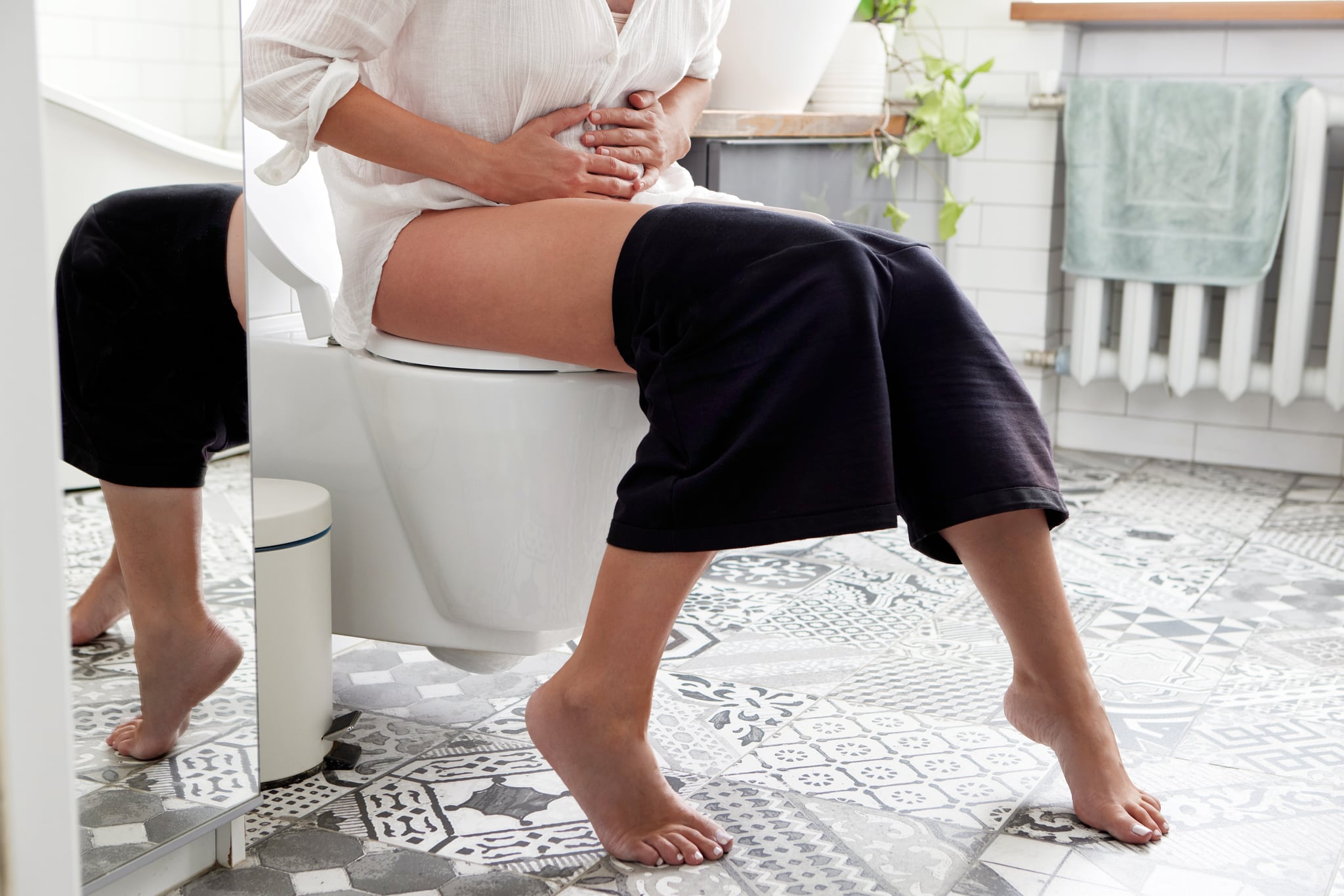Female suffers from diarrhea hand holding stomach on toilet bowl. 