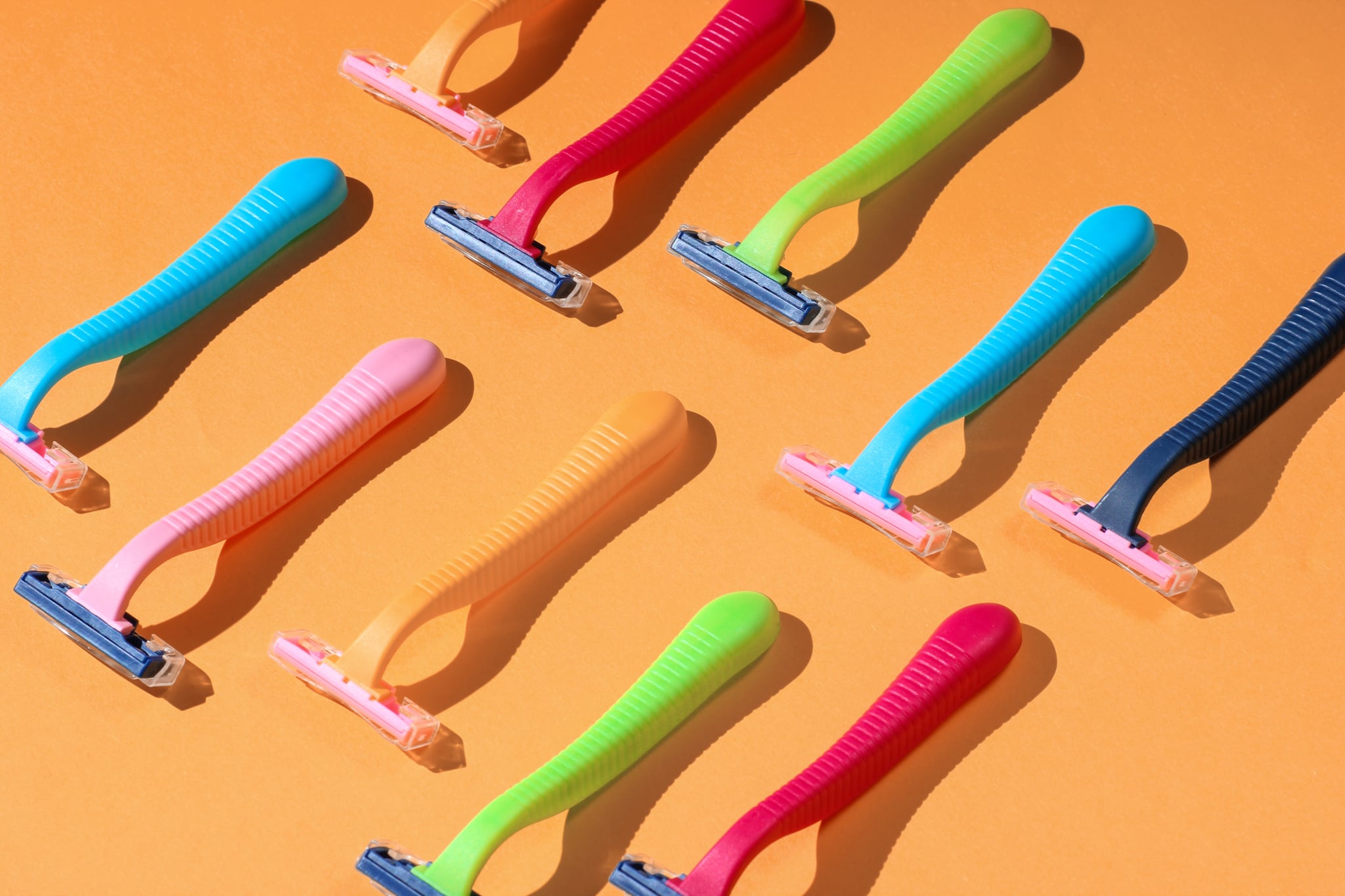 Beauty and fashion pop art concept. Many colored plastic razors on orange background. Minimalism