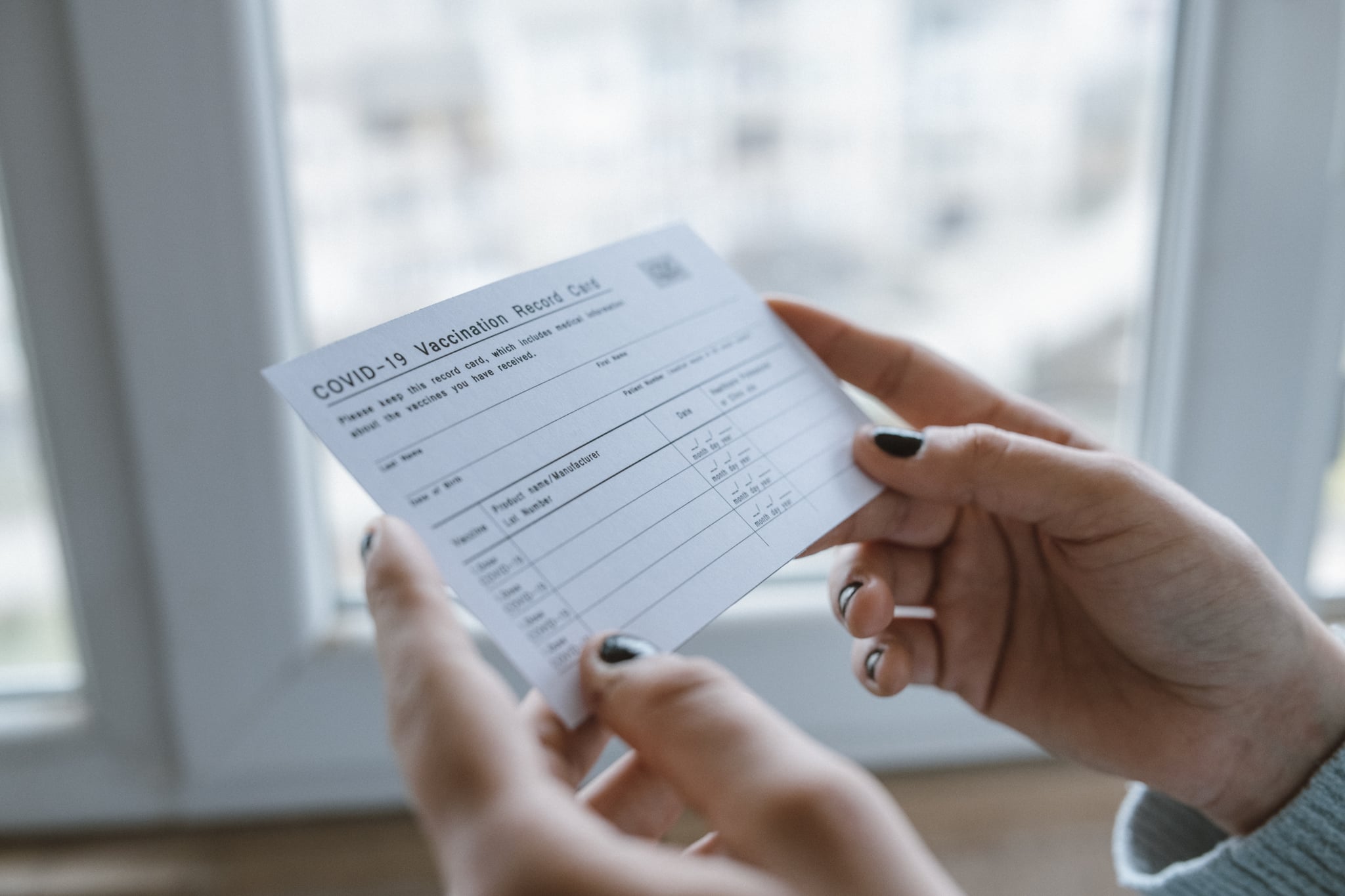 Close up of cropped female hands holding COVID-19 vaccination record card.