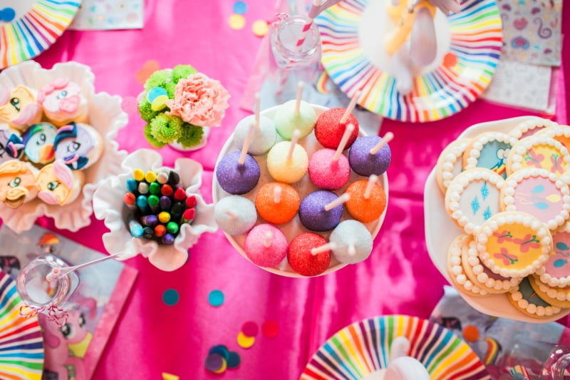 I created fun desserts around this theme without making anything that was super time consuming or difficult.  Ally’s favorite pony is Rainbow Dash, so I came up with Rainbow Dash Cutie Mark Krispies, made using a basic Rice Krispies recipe but dividing the batch and using rainbow colors. I cut them into Rainbow Dash’s cutie mark shape and added mini marshmallow “clouds”.  They were a hit, especially among our gluten-free guests.
Another simple treat were the Rainbow Power Pops, basic cake pops but dipped and sprinkled in every color of the rainbow.  Piece of cake plus big crowd pleaser equals recipe success.  (I have lots of cake pop recipes in my book if you need ideas.)