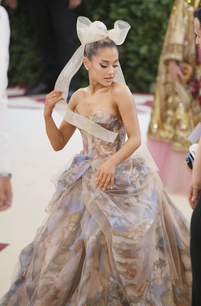 Ariana Grande's lavish gown for the 2018 Met Gala was quite literally a work of art. The 24-year-old "No Tears Left to Cry" singer wore a princess-style Vera Wang gown with a romantic tulle overlay, a matching bow hair accessory, and elegant Butani diamonds. 
If the gown's print looks familiar, that's because it's Michelangelo's famous fresco "The Last Judgment," which covers the altar wall of the Sistine Chapel in Vatican City. So don't say she didn't stick to the "Heavenly Bodies" theme! Ahead, see more pictures of Ariana's dress that are sure to delight art history buffs and fashion fans alike.