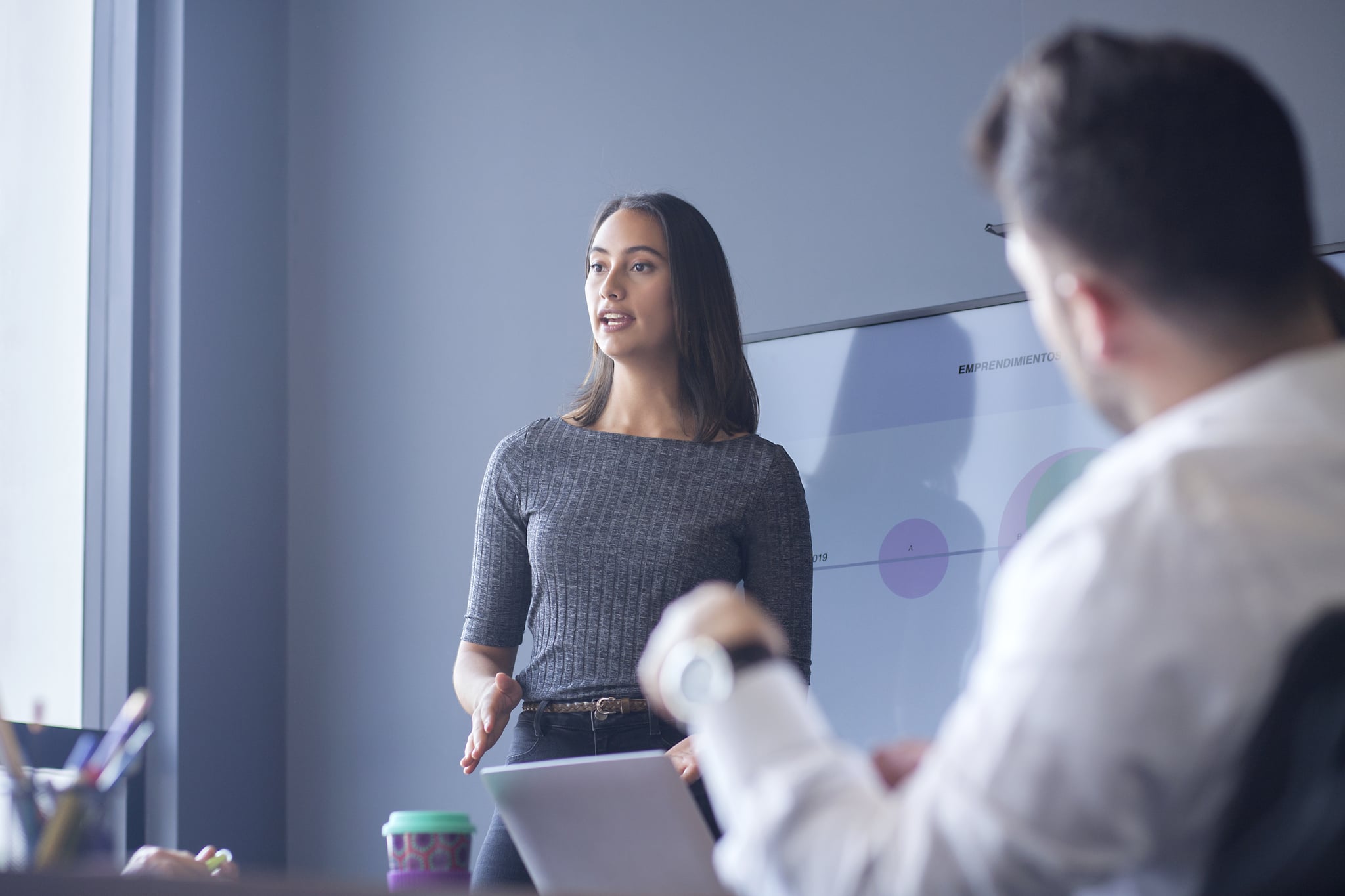 Woman of Latin ethnicity between 25-35 years is at work conducting a conference for her co-workers in the boardroom