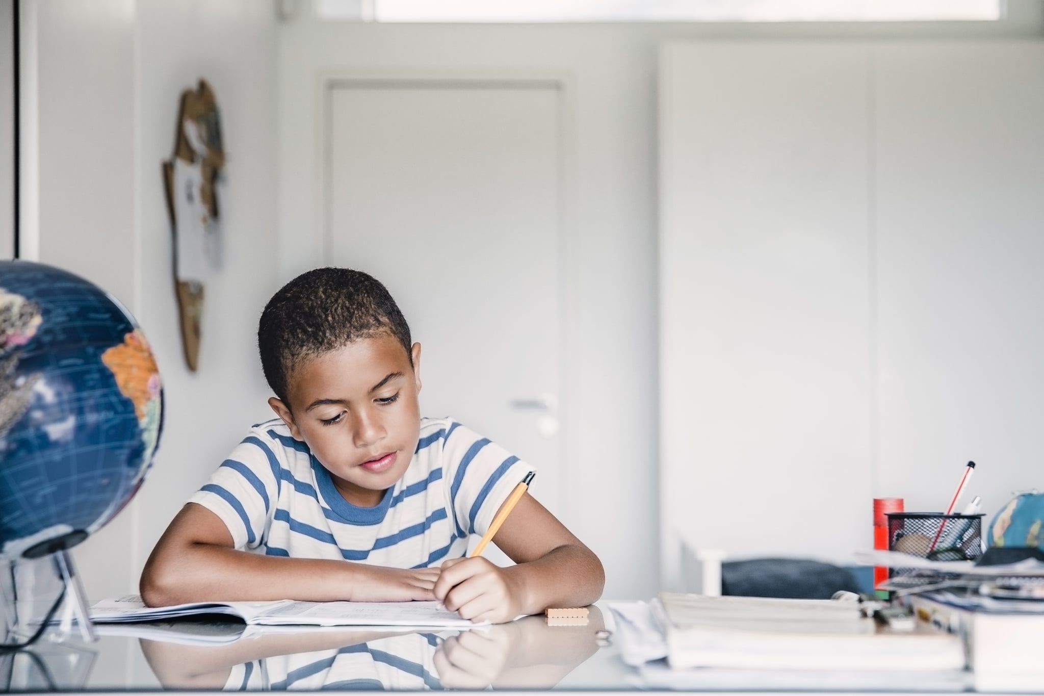 Cute boy studying at table in house