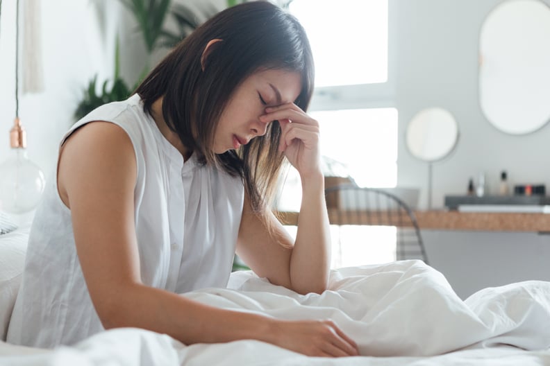 年轻女人触摸鼻子的桥梁来缓解头痛在床上歇息的时候。