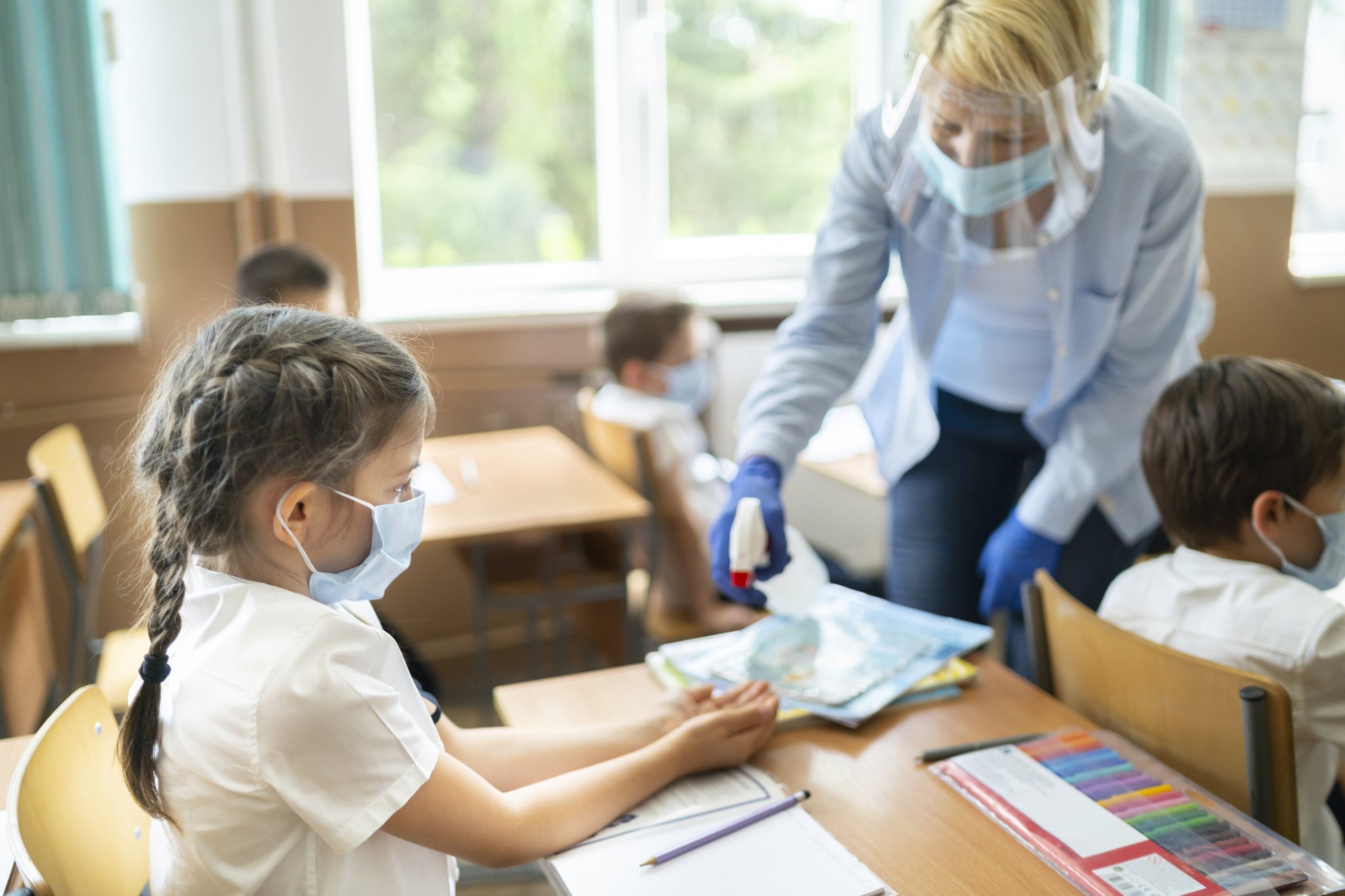 Service staff disinfecting hands of a girl in the classroom