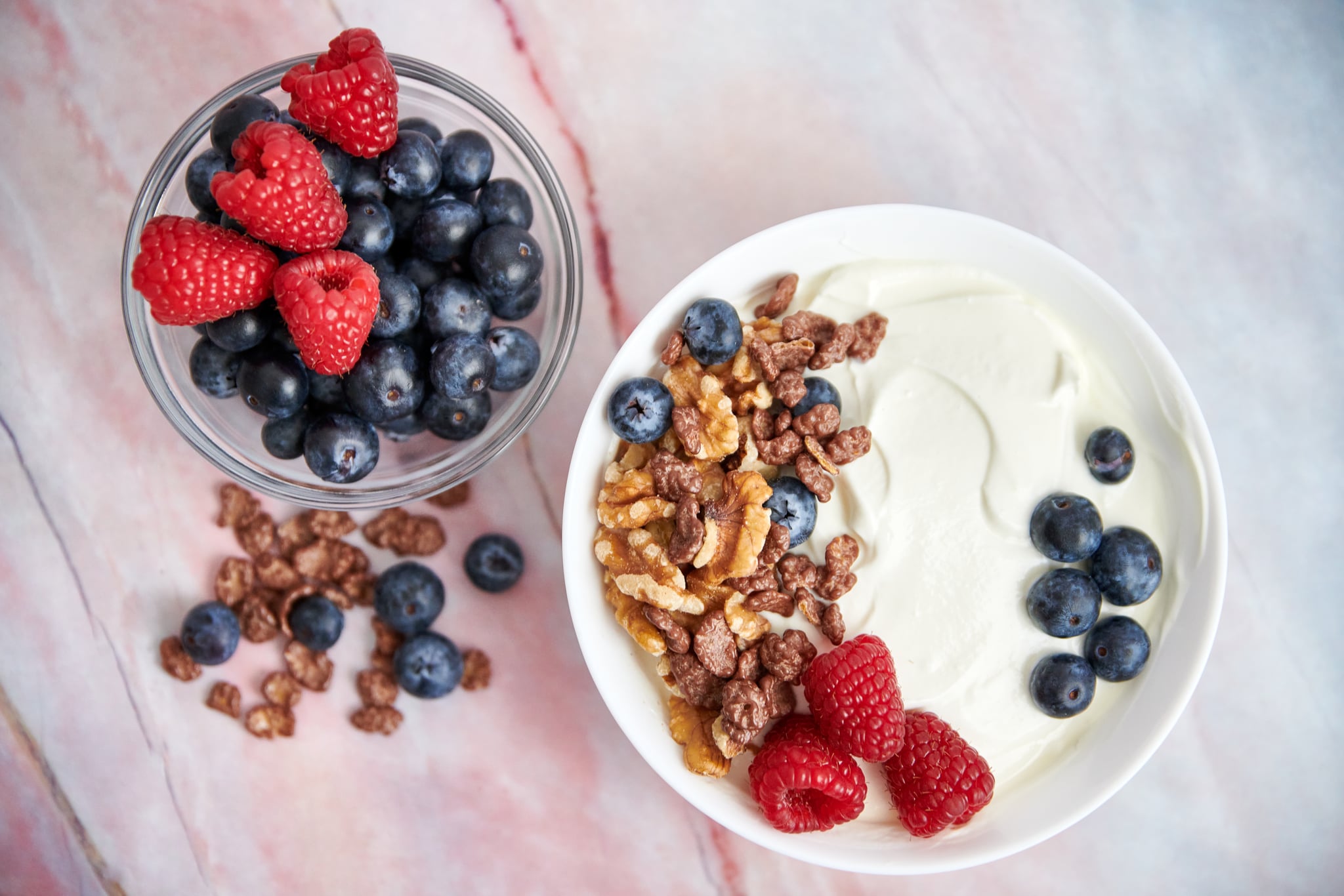 Bowl with dry yogurt, nuts, cereals, blueberries and fresh raspberries on a marble background. top view