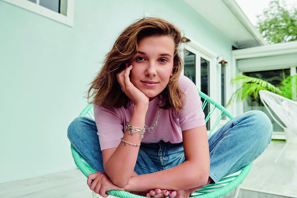 Millie Bobby Brown codesigned a jewellery collection with Pandora Me inspired by some of her sweetest memories of the summer. The Stranger Things star launches her five-piece capsule collection exclusively at Pandora on Thursday, 2 July.
Millie recently became an ambassador for the iconic jewellery brand, and her exciting new collection includes four dangle charms and one earring. The colourful charms feature a pink flamingo, pink starfish, yellow-and-green pineapple, and a blue ocean wave, where the earring is a single stud with a pink sea turtle — because one of Millie's favourite seaside activities is watching turtles swim. Of the charms, Millie says that "all of the symbols I chose are my absolute favourite parts of summer, and each charm holds a fun memory or meaning to me." Each charm is made of hand-finished, 98 percent recycled sterling silver with colourful cubic zirconia crystals, made in Pandora's eco-factory in Thailand.   
Ahead, take a sneak peek at the Millie Bobby Brown and Pandora Me jewellery capsule collection ahead of the official launch on Thursday, 2 July.