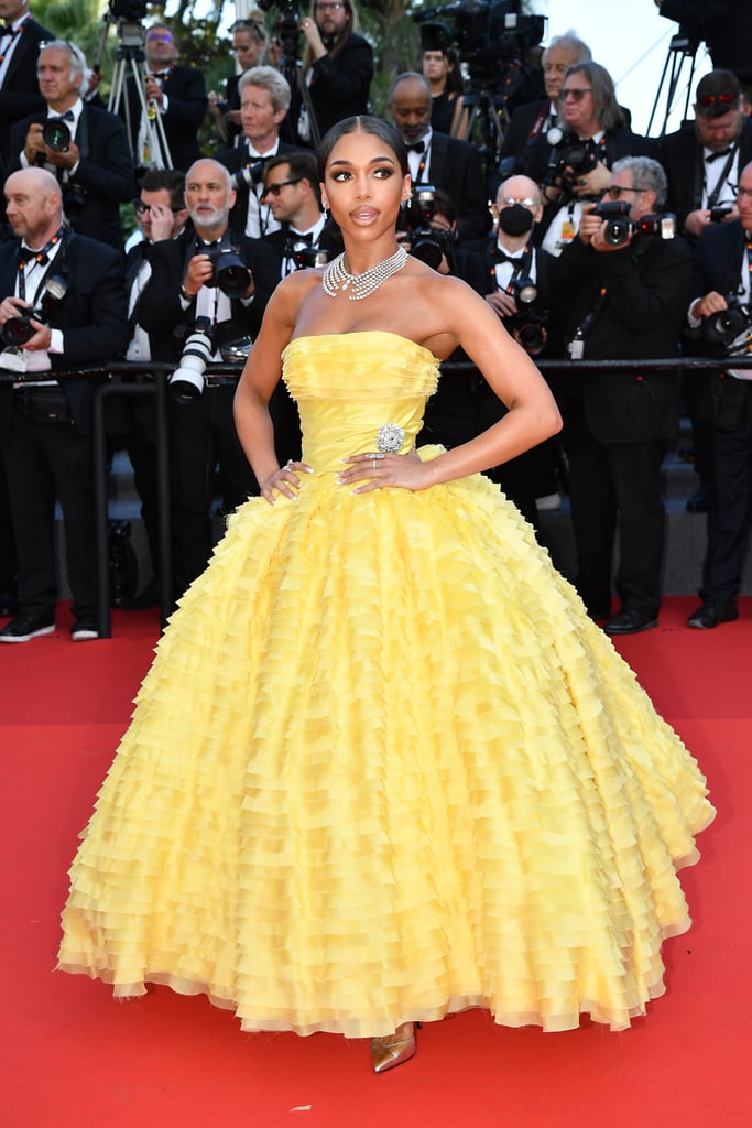 Lori Harvey just executed this year's Met Gala theme at the opening ceremony of the 2022 Cannes Film Festival. Harvey hit the red carpet at Palais Des Festivals in a commanding strapless ball gown that exuded "Gilded Glamour." The ruffled gown, which is Look 40 from Alexandre Vauthier's spring 2020 couture collection, featured a frayed bodice wrapped in layers of spooled ribbon and held together by a shimmering diamond brooch on the left hip. The voluminous skirt flared in tiers of buttery-yellow ruffles framing Harvey's waist, reaching down to an inch above the red carpet to give us a glimpse of her pointed gold heels. She styled the look with a layered Messika Paris High Jewelry Shards of Mirror Necklace, Illusionistes Diamond Clip Earrings, a Danseurs Aériens Two Finger Ring, and a Toi & Moi Ring. 
In a sea of suits and breezy maxi dresses, Harvey illuminated the red carpet, keeping firm focus on the whimsical garment with her relatively minimal accessories. The dress's buttery sheen caught the sunlight beautifully, and her refined beauty look — a french manicure, a sleek bun, and a glossy two-toned lip — gave Harvey's full ensemble a total air of regality. Sophisticated, sleek, and perfect for a day out on the French Riviera.
Harvey's actual Met Gala look was a crisscross Michael Kors dress in black with a flowing train and a daring ab-baring diamond cutout. "Thank you, @michaelkors, for letting me be one of your muses for the evening! What a moment! I don't think I'll ever be over this stunning dress you made for me," Harvey gushed on Instagram following the event.
See Harvey's gorgeous ball gown at the Cannes Film Festival from all angles ahead.

    Related:

            
            
                                    
                            

            See Every Breathtaking Look From the 2022 Cannes Film Festival