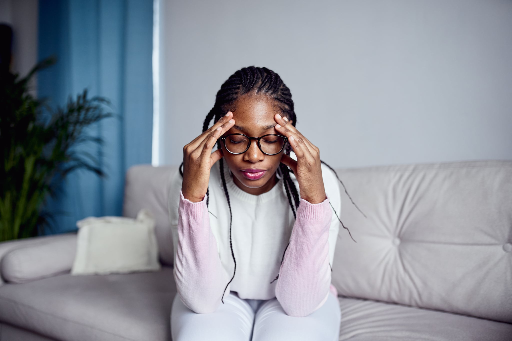 一个年轻的女人坐在家里的沙发上，双手抱着头。健康问题的概念，头痛或压力