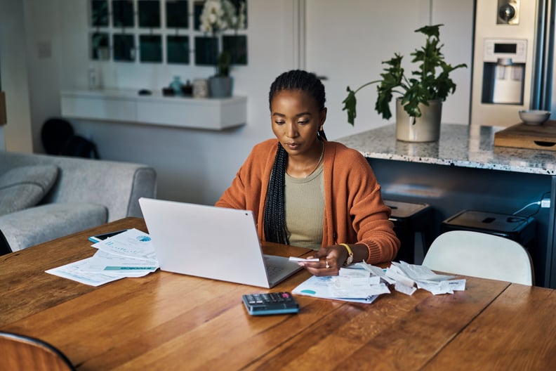 Woman working on a budget on the computer surrounded by bills and paperwork.