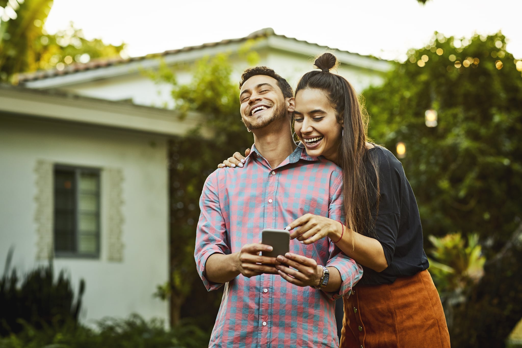 Cheerful couple looking at smart phone. Young man and woman are wearing casuals. They are having fun in back yard