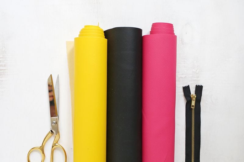 Supplies:

vinyl fabric in yellow, pink, and black
zipper
fabric scissors
fabric glue
X-Acto knife
emoji clutch template (right click to download)
round bowl or plate about 8" wide
binder clips (optional)
non-stick sewing machine foot (optional)
Chicago screw for handle (optional)