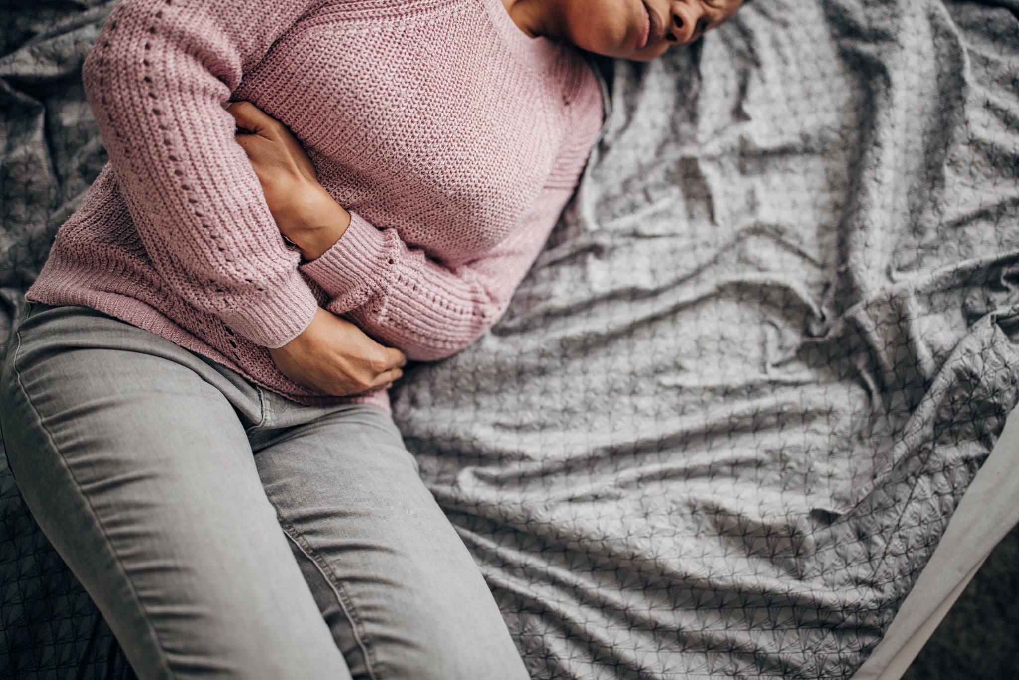 One woman, black woman having stomachache while lying on bed in her bedroom at home.