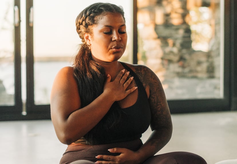 Una mujer medita con una mano sobre el pecho y la otra sobre el estómago.