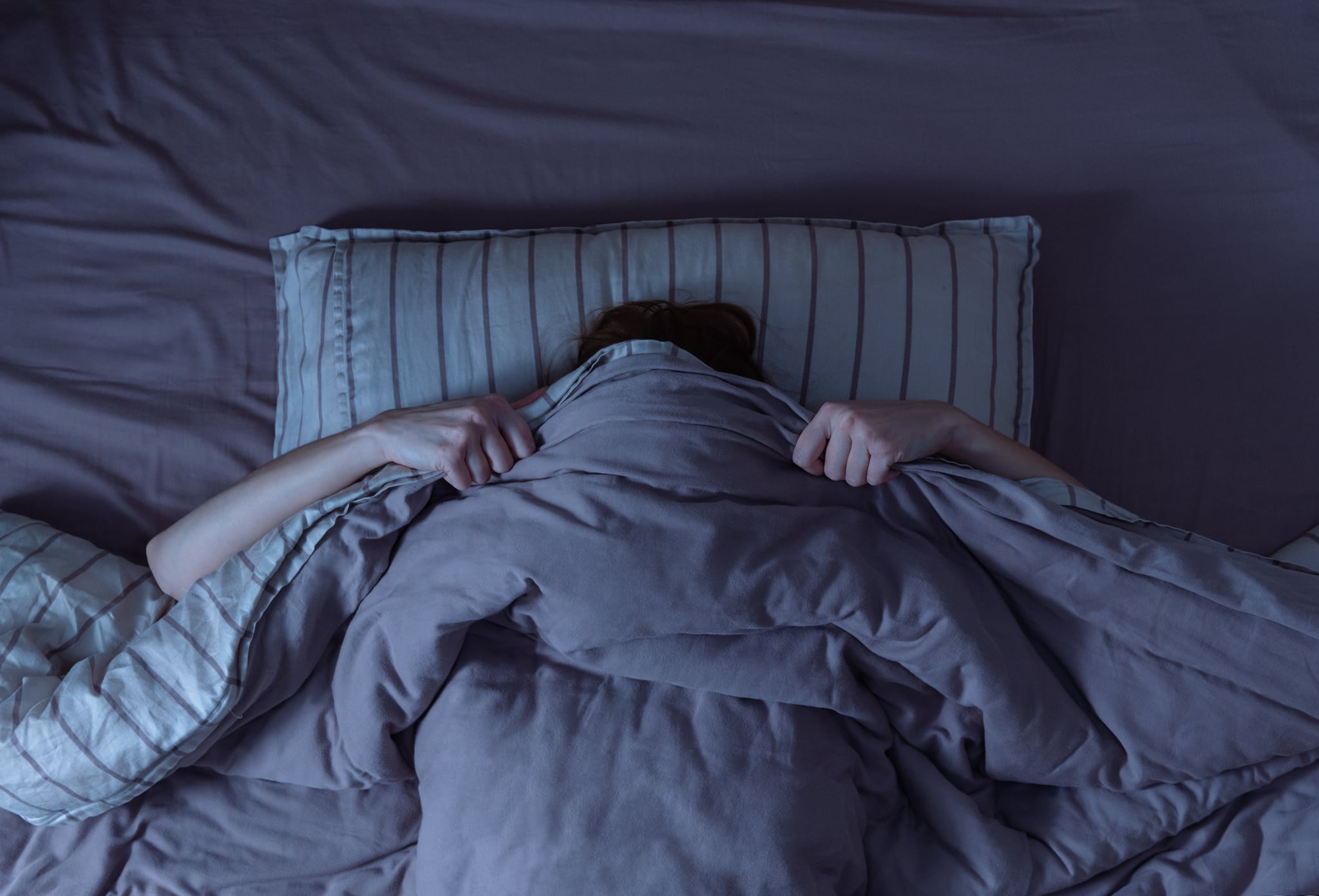 Top view of woman in bed covering her face with blanket, scared by melatonin nightmares.