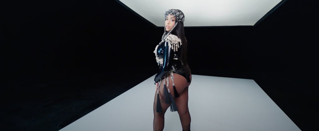 Jordyn Woods makes a cameo wearing a tassel-adorned latex bodysuit, fishnets, and a shiny headpiece.