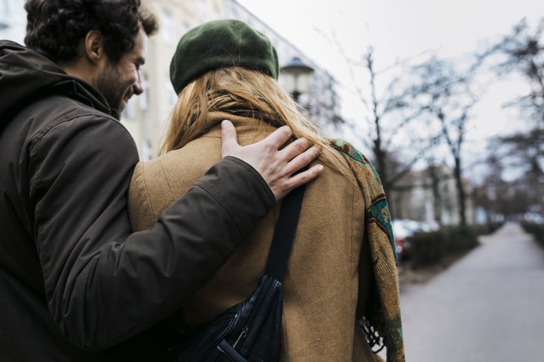 A man smiling with his arm around his girlfriend while out walking in the city together.