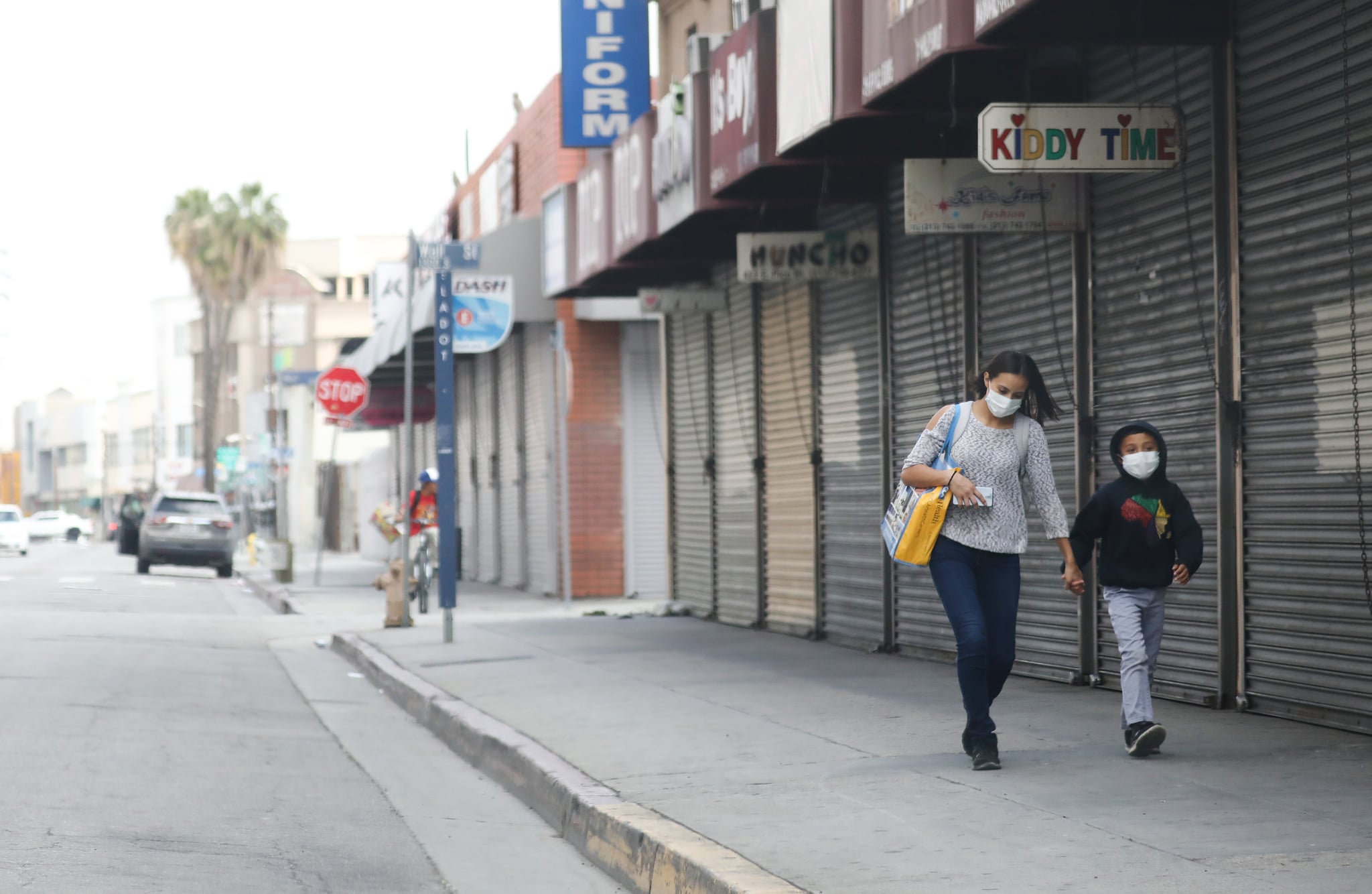 LOS ANGELES, CALIFORNIA - APRIL 04: A woman and child wear face masks while walking past shuttered downtown shops amid the coronavirus pandemic on April 4, 2020 in Los Angeles, California. The U.S. COVID-19 death toll has now surpassed 8,000. (Photo by Mario Tama/Getty Images)