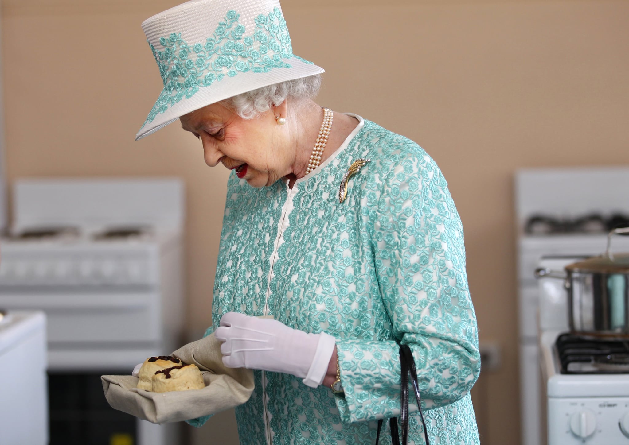 Britain's Queen Elizabeth II looks at homemade scones as she visits the kitchen at Clontarf Aboriginal College in Perth on October 27, 2011. The queen, who arrived in Perth on October 26, will officially open the 54-nation Commonwealth Heads of Government Meeting (CHOGM) on October 28 where revamping succession to the British throne will be discussed, concluding a 10-day tour of her antipodean realm.    AFP PHOTO / POOL / SHARON SMITH (Photo credit should read SHARON SMITH/AFP via Getty Images)