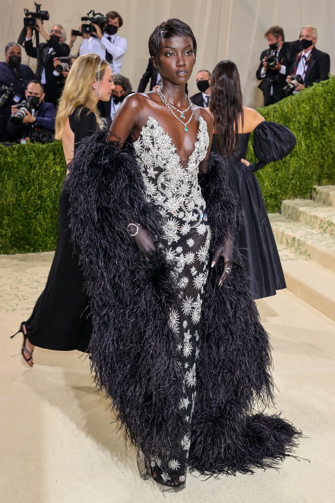 The 2019 Met Gala's "Camp" theme still had a prominent influence on many of this year's attendees, but many of those who understood the 2021 Met Gala's "In America" assignment took inspiration from some of history's most influential stars. Much like Yara Shahidi showing up in a head-to-toe Dior outfit inspired by Josephine Baker, model Anok Yai also gave a nod to the 1920s entertainer and civil rights activist. Channeling peak "Old Hollywood" glam, Anok posed on the Costume Institute steps in a figure-hugging Oscar de La Renta dress from the Spring 2022 collection. While Anok and Yara's outfits couldn't have been more different, both paid an honorable tribute to the Jazz Age star. 
Described as a "skimming celestial crystal gown" by the Oscar de La Renta Instagram page, the dress features a plunging neckline and crystal designs in the shape of flowers and stars. Stylist Carlos Nazario paired the look with Giuseppe Zanotti heels, matching sheer black opera gloves, and an oversized shawl bursting with black feathers, which Anok pulled off effortlessly. Looking left or looking right, the model nailed every single pose and came out looking like a star in her own right from every angle. Prepare to be dazzled by Anok's crystal-covered dress and impeccable poses ahead. 

    Related:

            
            
                                    
                            

            Timothée Chalamet&apos;s Converse Were Just 1 Part of His Very Chic Met Gala Outfit