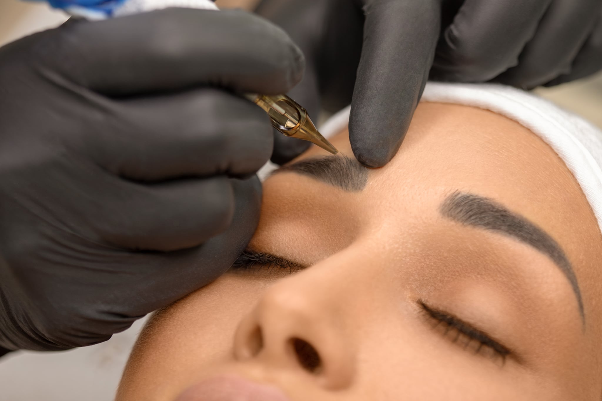 Make up artist applying permanent make up on eyebrows at beauty treatment. Beautician contouring and shading young woman's eyebrow with special tool.