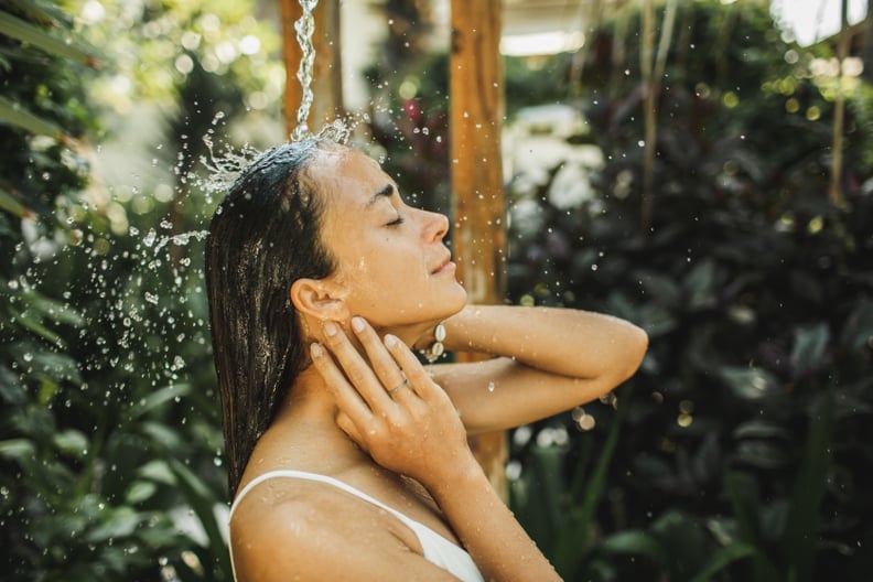 A woman in white swimsuit relaxing and refreshing under an outdoor shower.