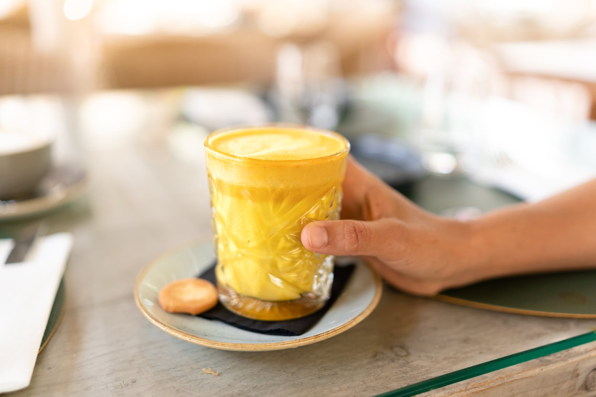 Woman holding golden milk in a clear glass on a wooden table.