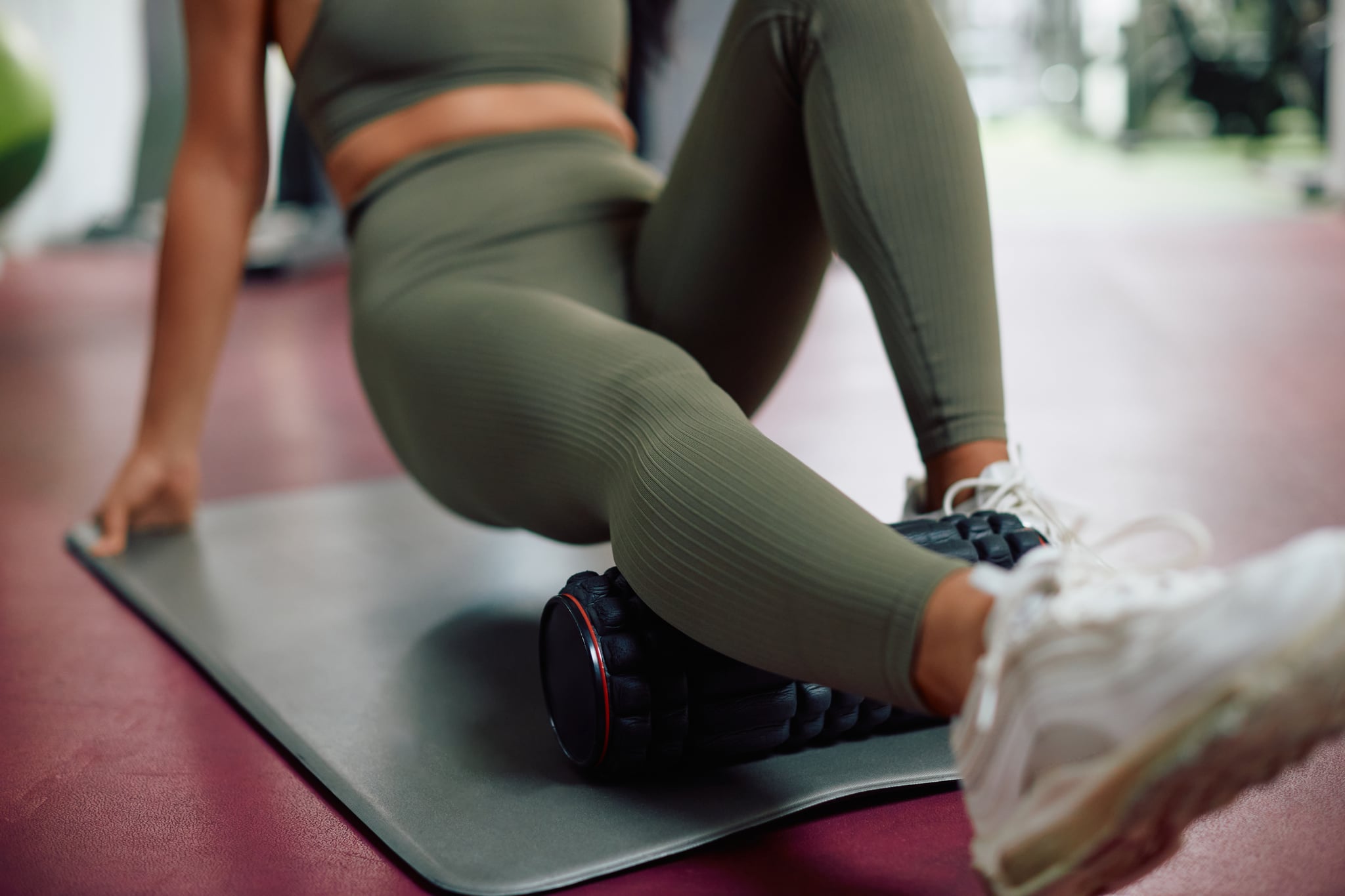 Close-up of athlete massaging her leg with foam roller in a gym.