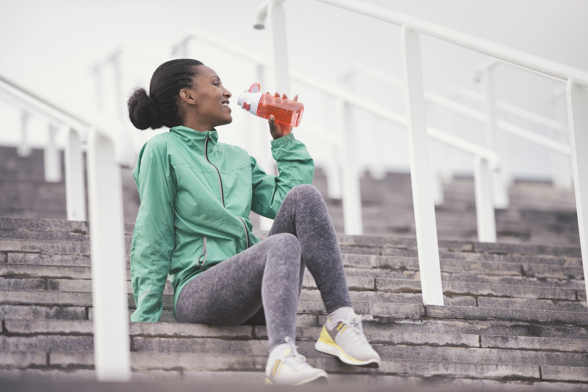 Low angle view of a young athletic woman taking a break from running exercises, drinking water from a plastic refillable bottle.