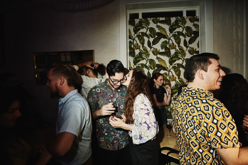A pair of adults whispering into each others' ears and flirting at a house party. 
