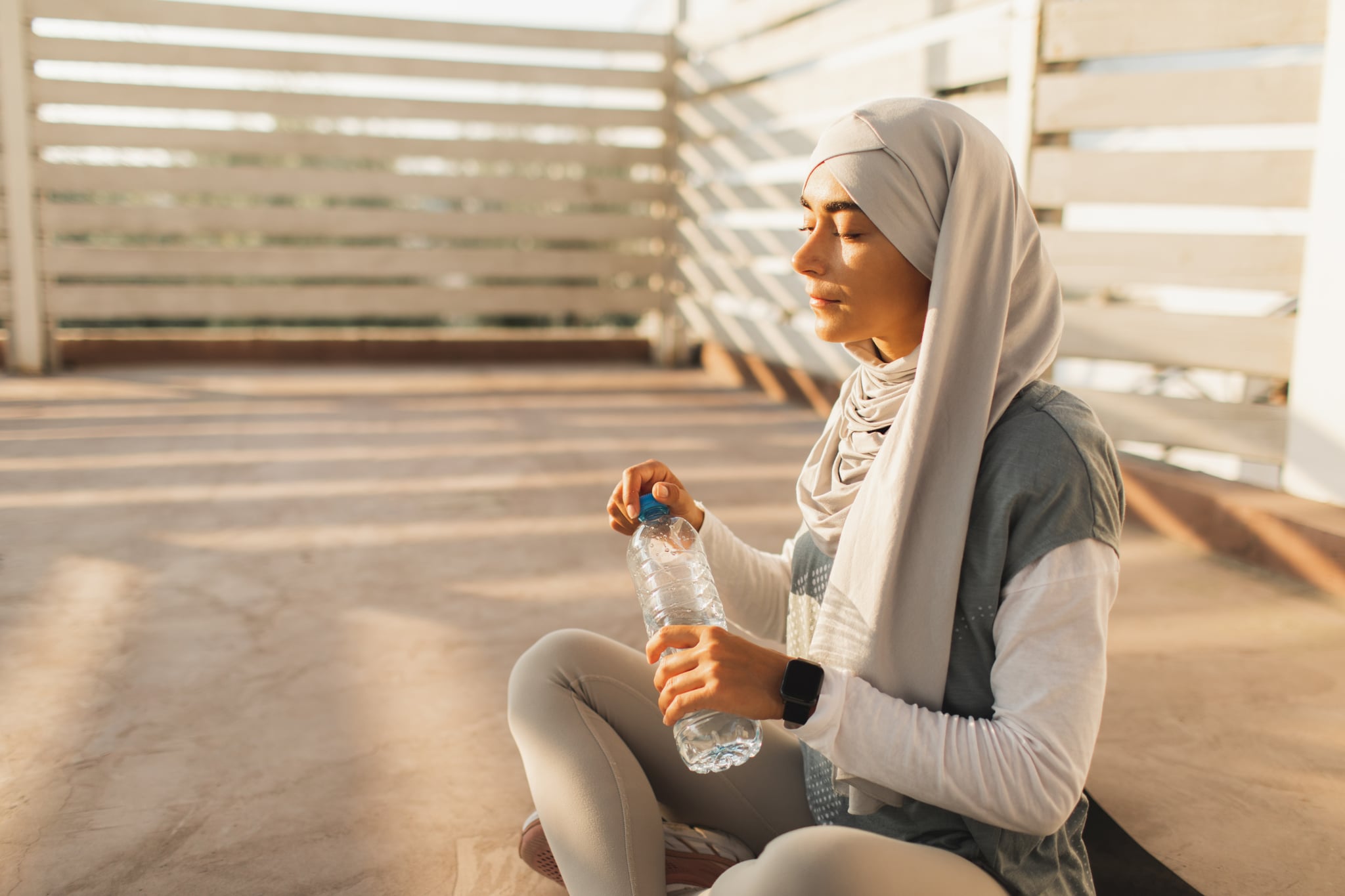 Healthy and active lifestyle of muslim girl in hijab wondering if she can drink water during ramadan. Training outdoors. Drinking water in plastic bottle. Hydration in sport.