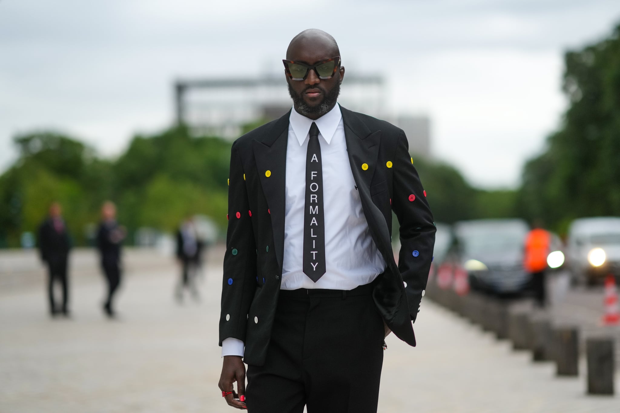 PARIS, FRANCE - JULY 05: Virgil Abloh wears a white shirt, a black tie with 'A Formality' slogan, a black blazer jacket with multicolored buttons embroidered, black flared suit pants, a red ring, a gold watch, butterfly sunglasses, outside Louis Vuitton Parfum hosts dinner at Fondation Louis Vuitton, during Paris Fashion Week - Haute Couture Fall/Winter 2021/2022, on July 05, 2021 in Paris, France. (Photo by Edward Berthelot/Getty Images)