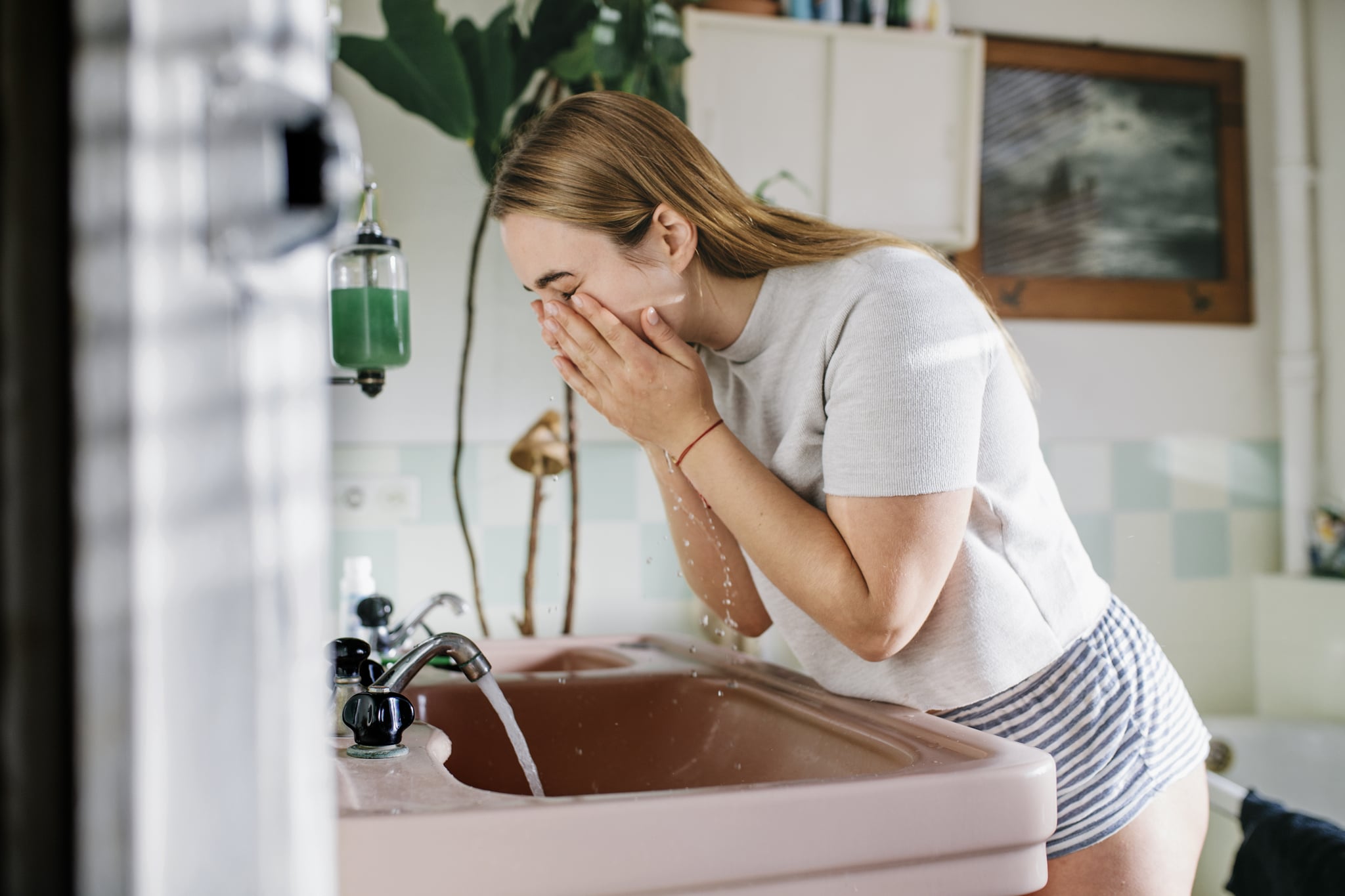 woman leaning over bathroom sink looking into mirror