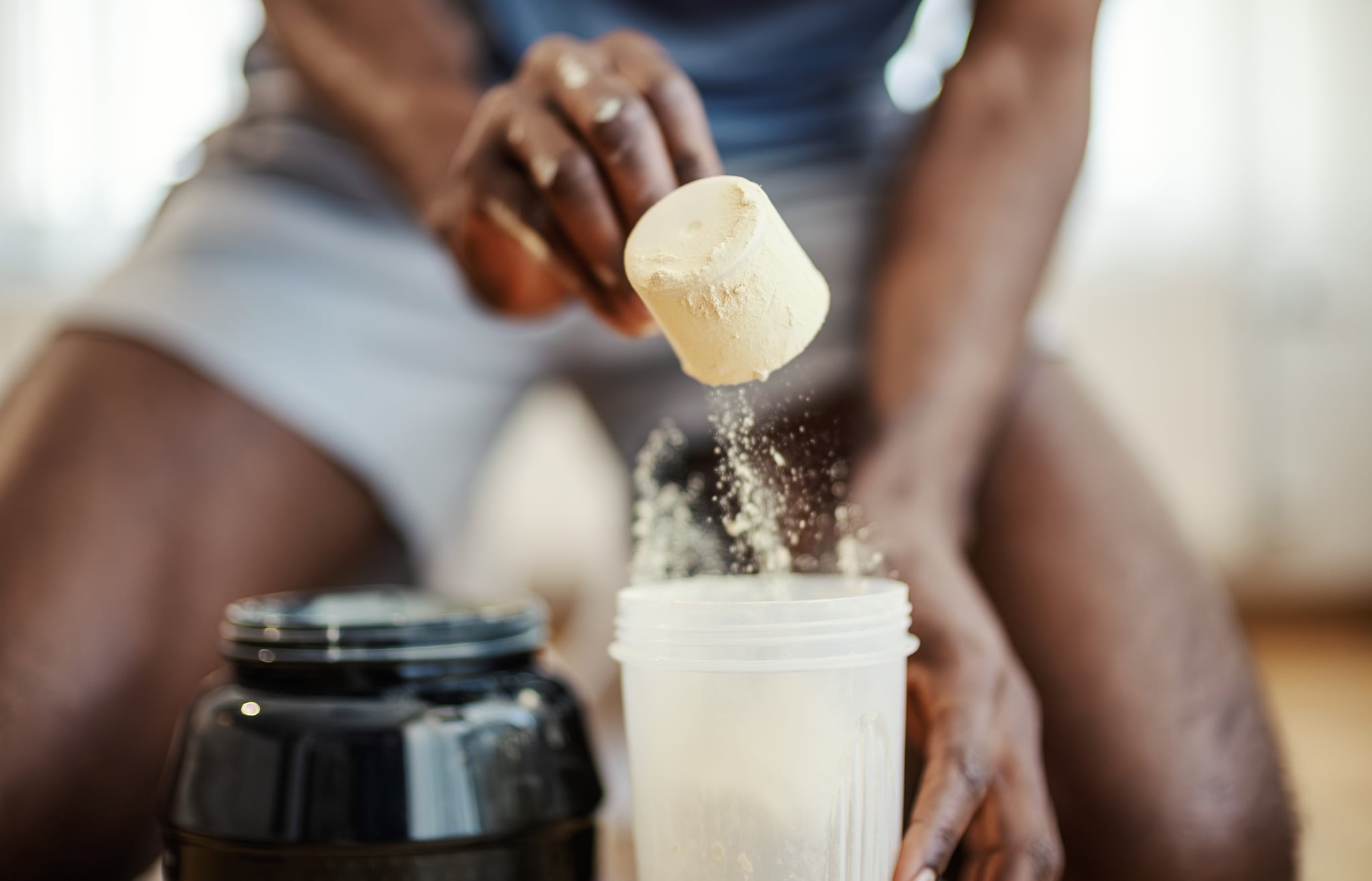 Young man preparing a nutrient supplement drink, pouring protein powder with a scoop into a shaker bottle.