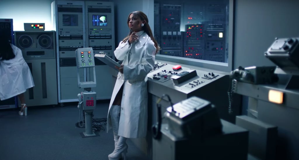 For her researcher role, Ariana went full monochrome in a white patent lab coat, over-the-knee platform boots, a turtleneck, and matching earrings.