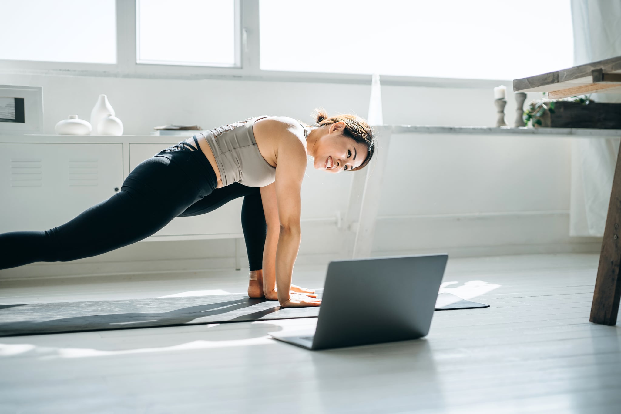 Young Asian woman doing online yoga class with laptop in the living room at home in the morning