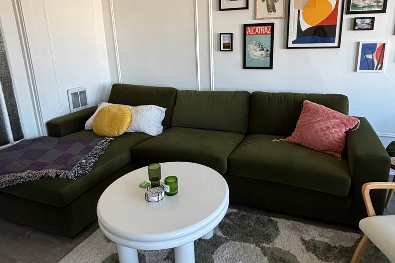 a photo of the albany park barton chaise sectional in a velvet green fabric is pictured, alongside a coffee table and gallery wall in an apartment.