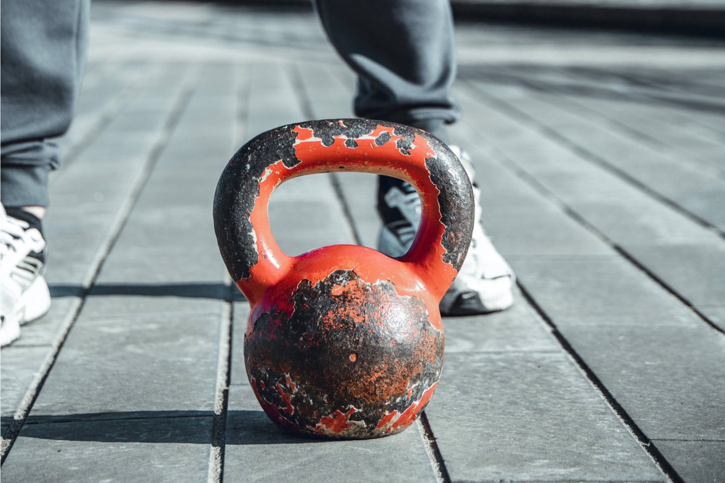 A rusted red dumbbell sitting on the ground with someone standing behind it.