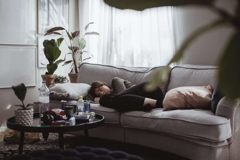 Sad woman laying on couch in messy living room.