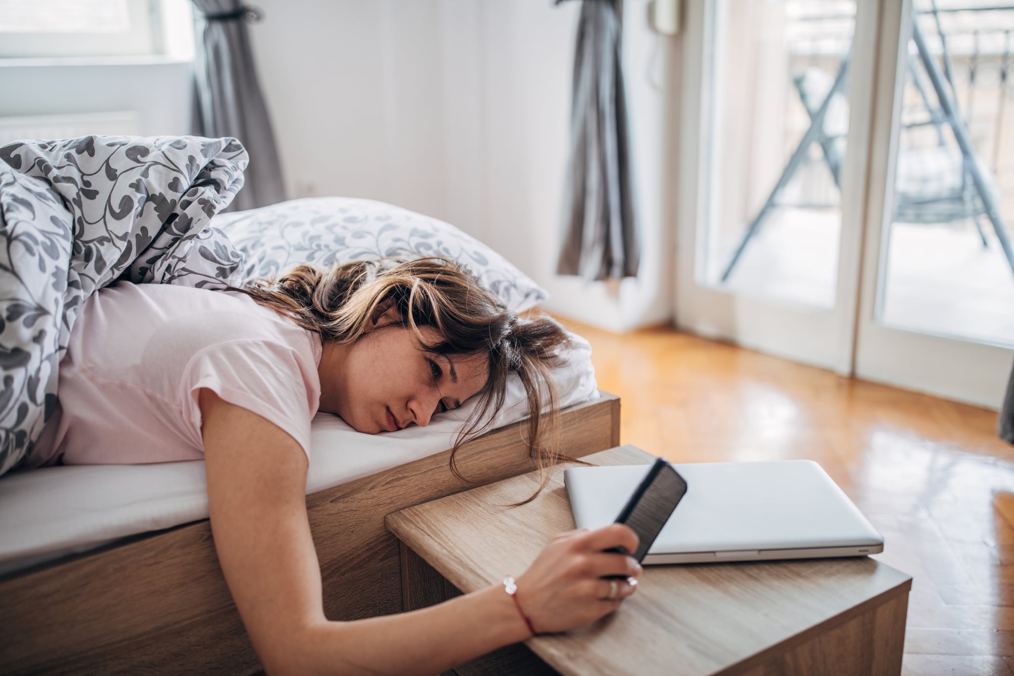 Young woman is waking up and looking at her smart phone.