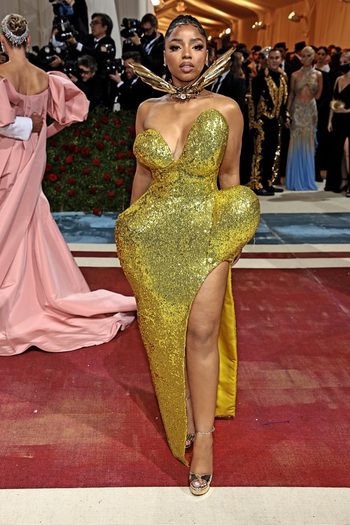 Chloë's dress at the 2022 Met Gala on Monday is proof that sometimes the sequel is even better than the original. After attending last year's gala alongside her sister, Halle Bailey, in matching Rodarte looks, Chloë walked the Met Gala red carpet solo in a plunging Area gown taken straight from the designer's couture spring/summer 2022 collection. Chloë's opulent ensemble featured a fitted bustier with asymmetrical cups and a sculpted skirt with exaggerated hip accents and a thigh-high slit. "i'm golden," she captioned photos of the shimmering gold dress on Instagram. 
Even though Chloë walked the red carpet by herself this year, her bespoke dress was adorned with enough sparkles to light up the entire event on her own. The "Treat Me" singer styled the look with a gilded feather choker reminiscent of the Golden Snitch from Harry Potter, matching rings, and a pair of peep-toe heels. Chloë kept her makeup soft and minimalist and opted to wear her hair in braids tied into a sleek ponytail that cascaded down her back. 
Just one week before the gala, Chloë tried the "emo girl" trend in a Burberry dress and matching baseball cap at Burberry and Riccardo Tisci's Lola bag event in Los Angeles. Other celebrities who channeled the "Gilded Glamour" theme at the 2022 Met Gala included Kim Kardashian in a vintage Marilyn Monroe ensemble, Billie Eilish in an upcycled corset dress by Gucci, and more. Ahead, check out Chloë's Area dress at the 2022 Met Gala.

    Related:

            
            
                                    
                            

            Normani Wanted to "Break the Rules" With Her Low-Rise Skirt at the Met Gala